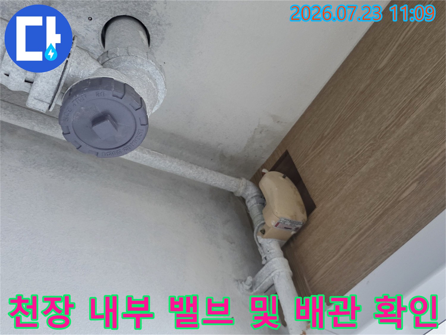 흰색 배관과 회색 플라스틱 밸브가 설치된 천장 내부 모습-누수 점검 중
