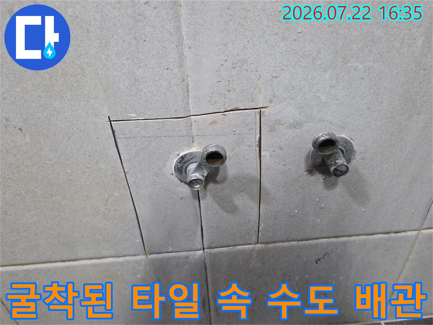 회색빛 타일 벽면의 일부를 사각형으로 파내어 노출시킨 금속제 배관 두 개