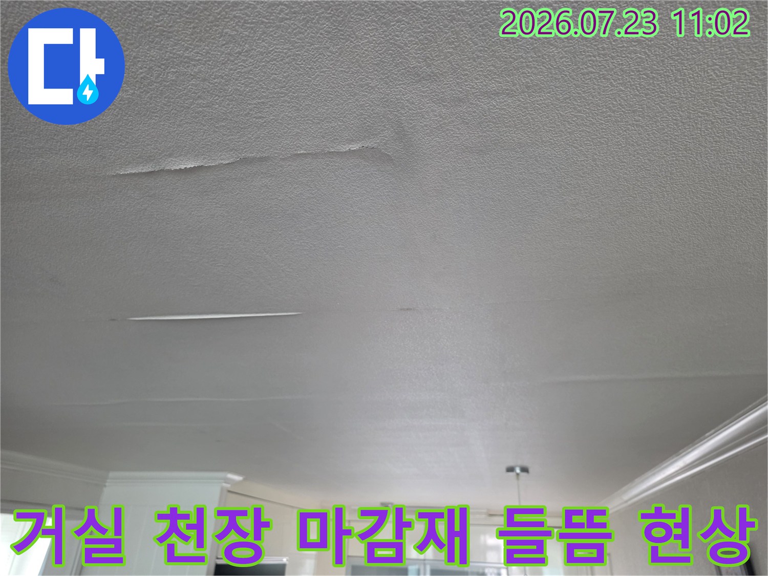 아파트 거실 천장의 흰색 마감재가 물기로 인해 부분적으로 들뜨고 균열이 생긴 모습