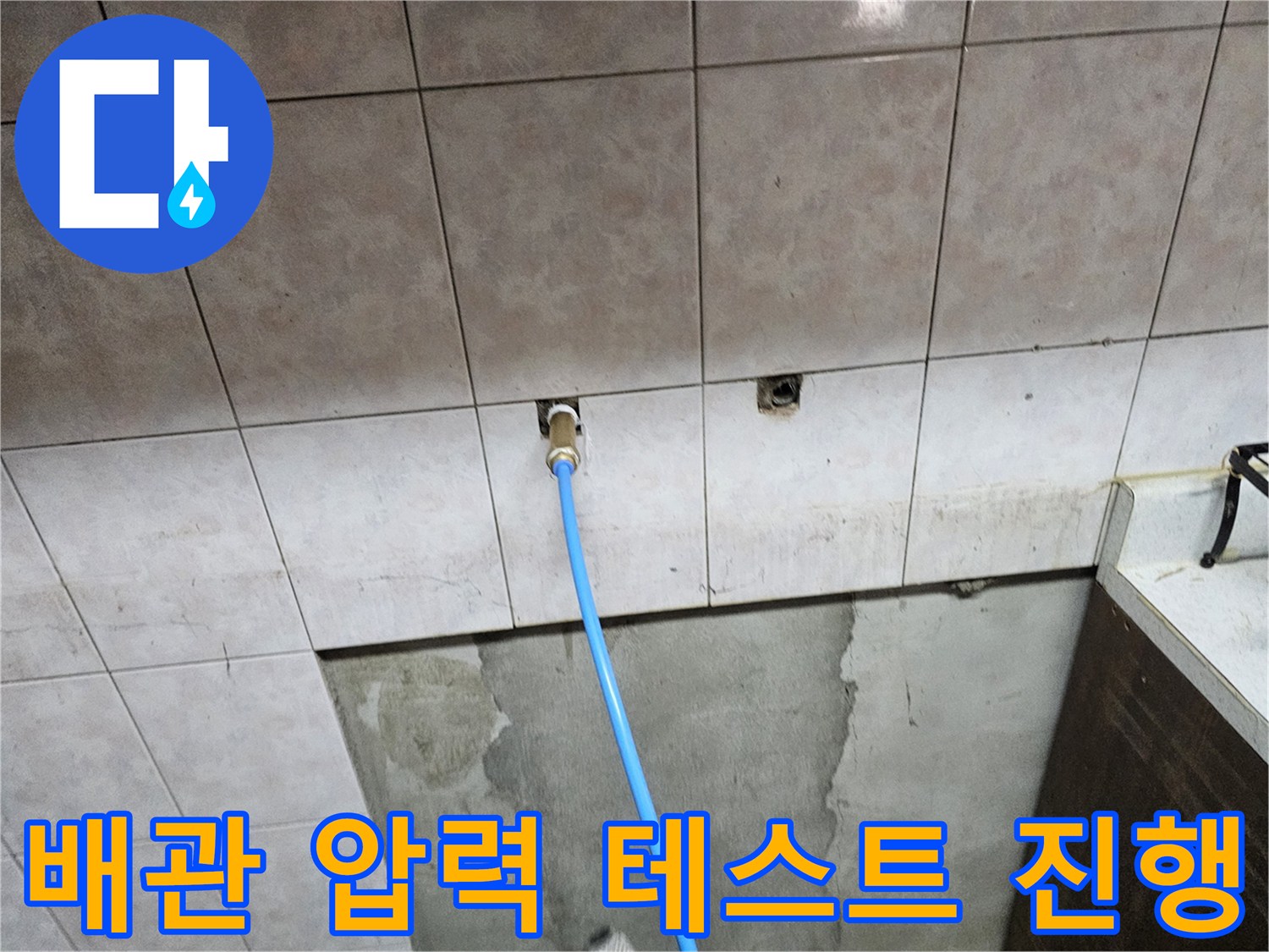 벽면 타일 사이 배관 입구에 연결된 파란색 점검용 호스