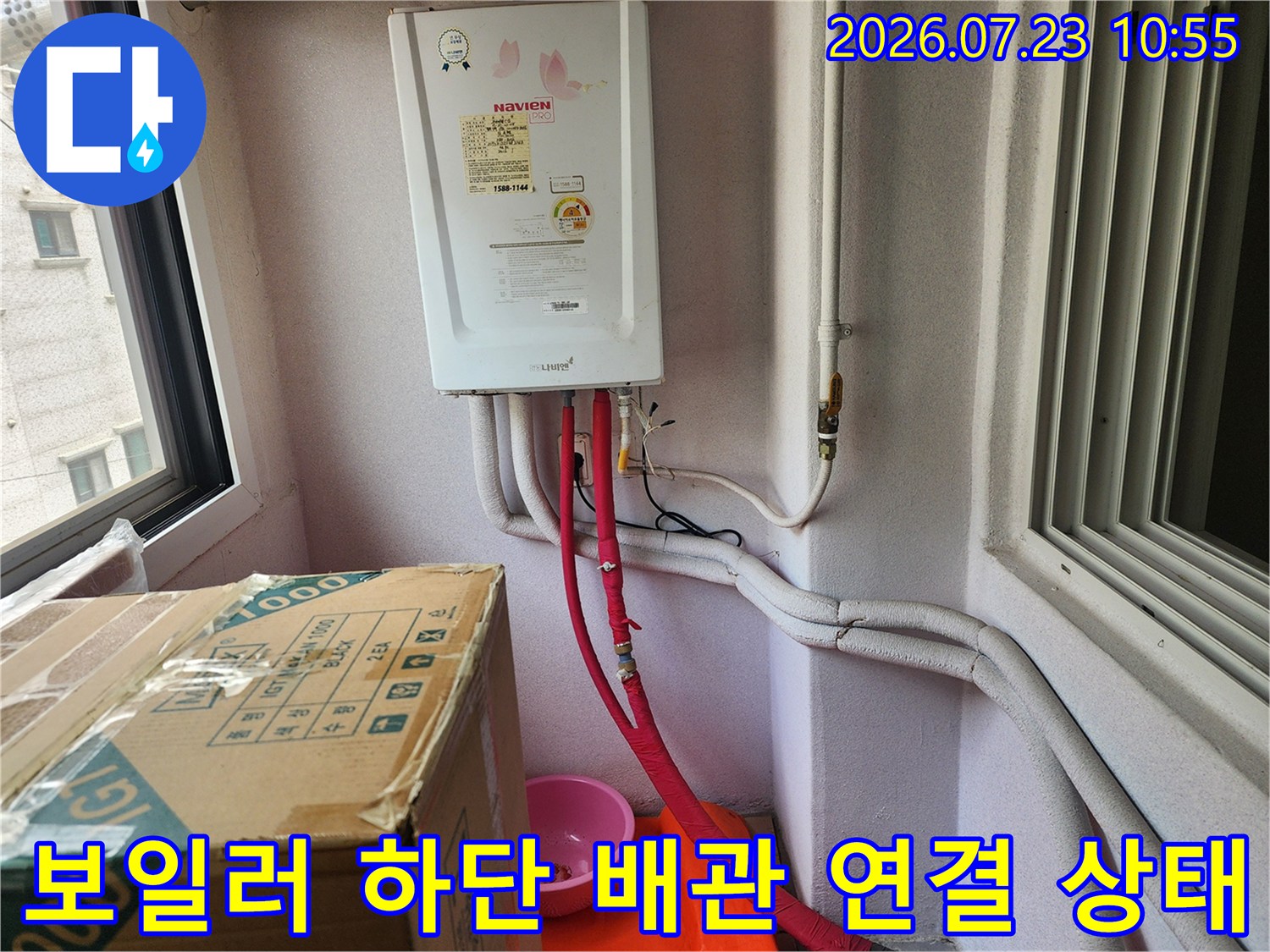 가스보일러 본체 아래로 연결된 붉은색 온수관과 흰색 보온재로 감싸진 다른 배관들의 모습