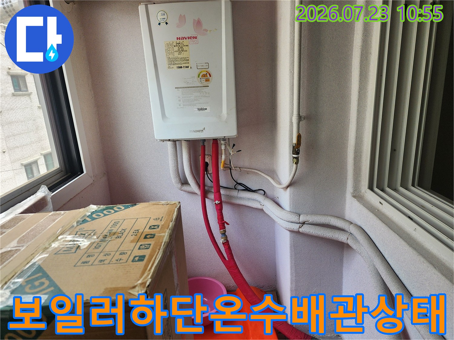 흰색 보일러 하단에서 바닥으로 연결된 빨간색 온수 배관과 흰색 보온재 배관 모습