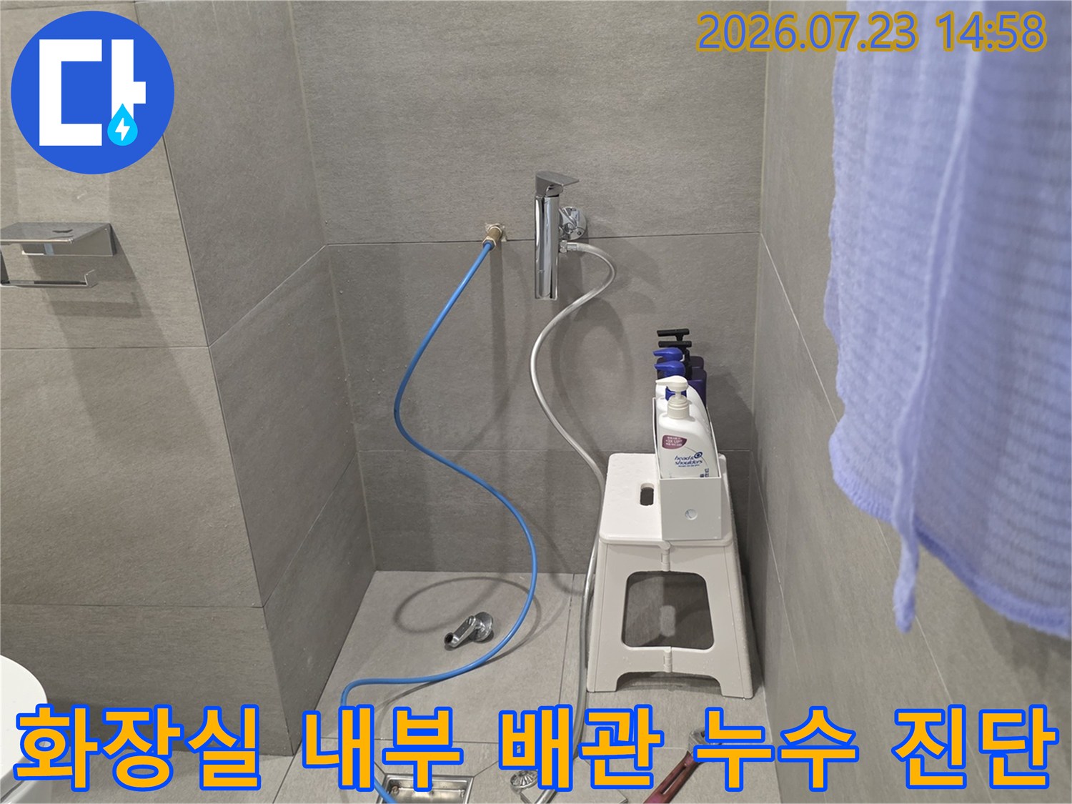 욕실 벽면 수전에 파란색 호스가 연결되어 있고 주변에 세정제와 의자가 놓인 사진