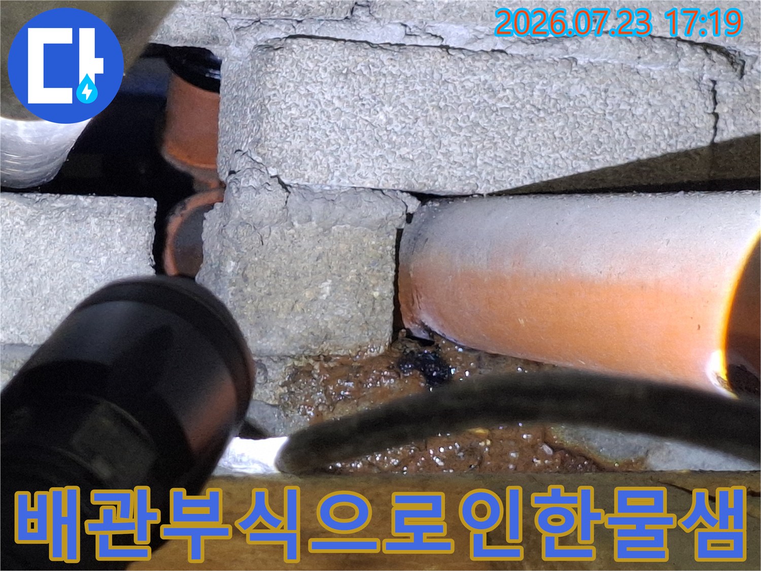 손전등 빛에 드러난-부식되어 구멍 난 오렌지색 배관과 주변의 젖은 바닥 상태