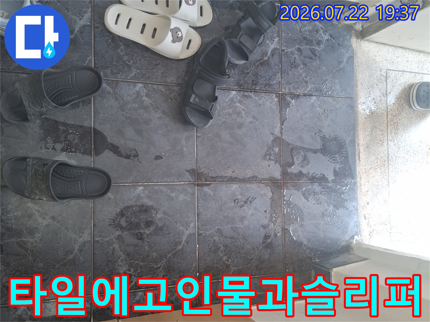 어두운 색상의 바닥 타일 위에 물이 흥건하게 고여 있고 그 주변에 여러 켤레의 슬리퍼가 놓여 있는 모습