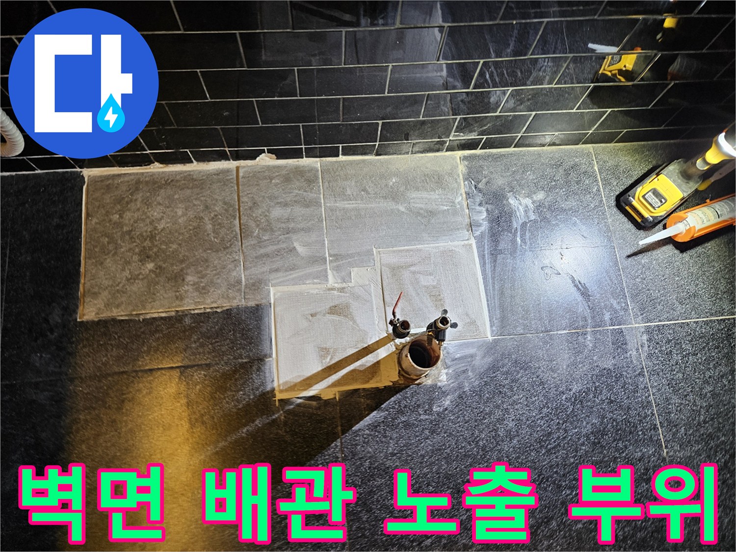 검은색 타일 벽면에 드러난 금속 온수 배관 연결부