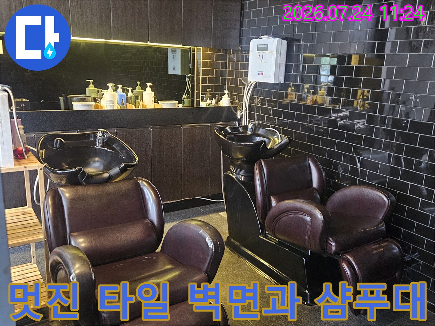 어두운색 가로 패턴 타일벽과 갈색 시트의 샴푸대가 배치된 실내