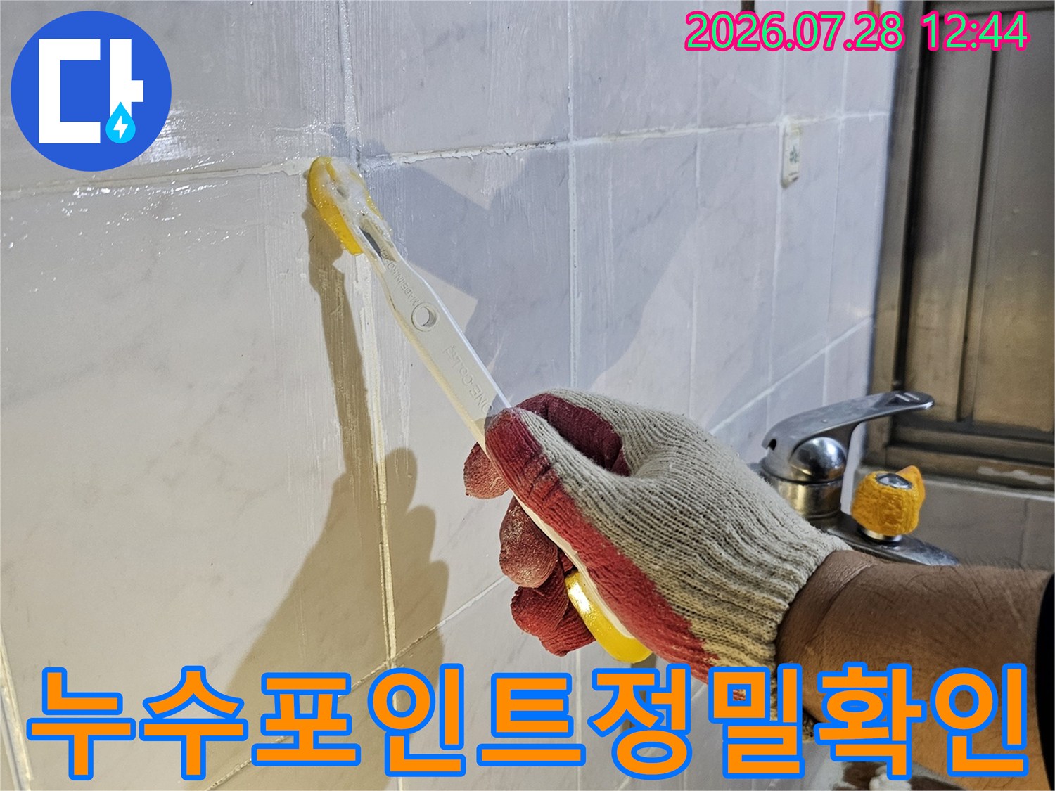 작업자가 타일 바닥 위에서 도구를 사용하여 배관 부위를 정밀하게 점검하는 모습