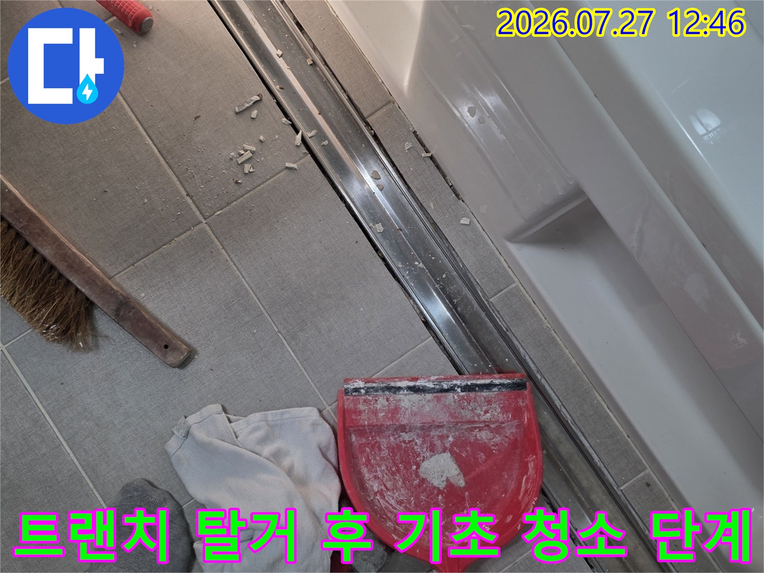 화장실 타일 바닥의 트렌치가 열려 있고 작업용 빨간 쓰레받기와 빗자루가 배치된 현장 사진