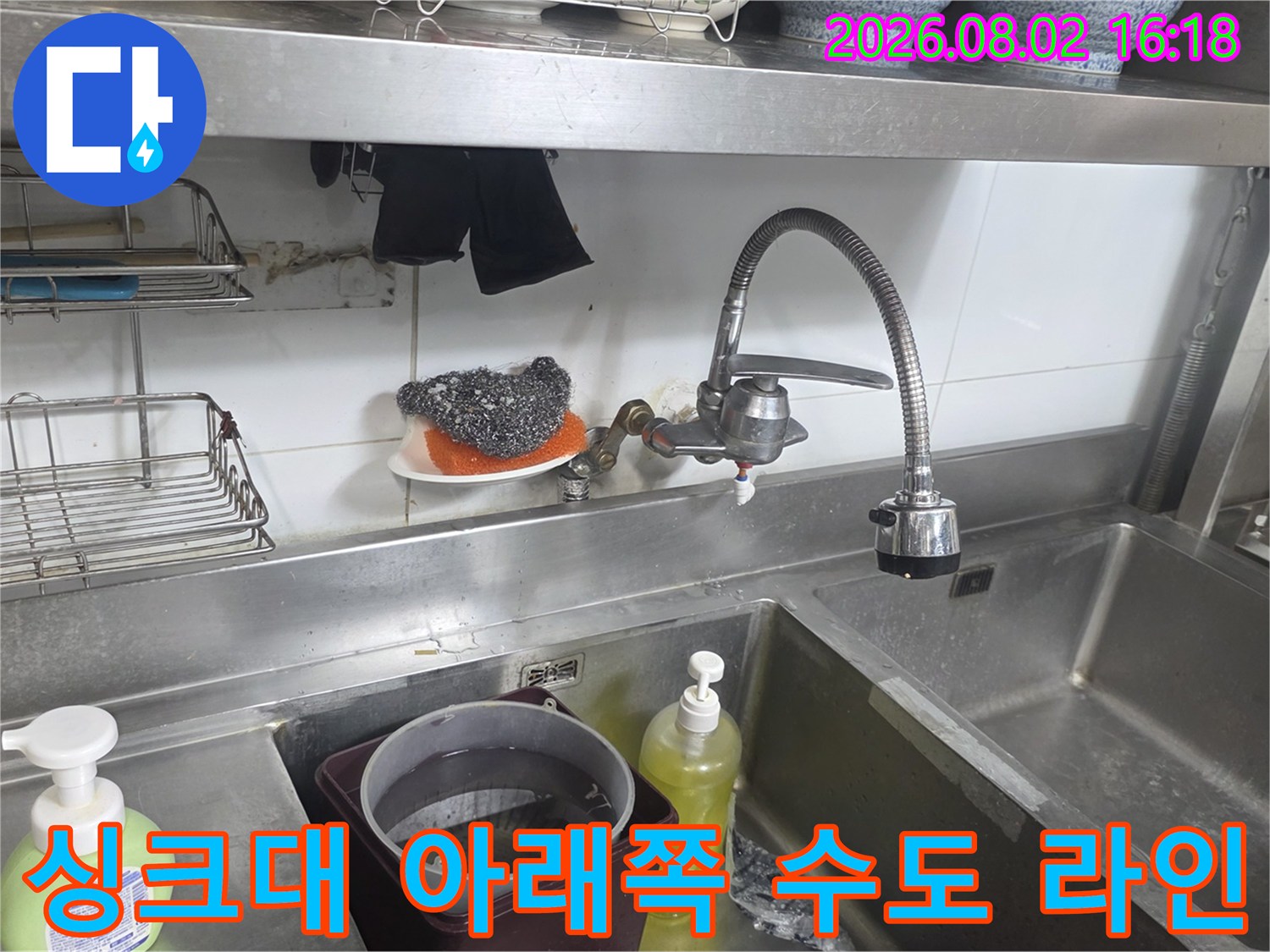 주방 싱크대 하단부에 설치된 수전과 노출된 배관라인