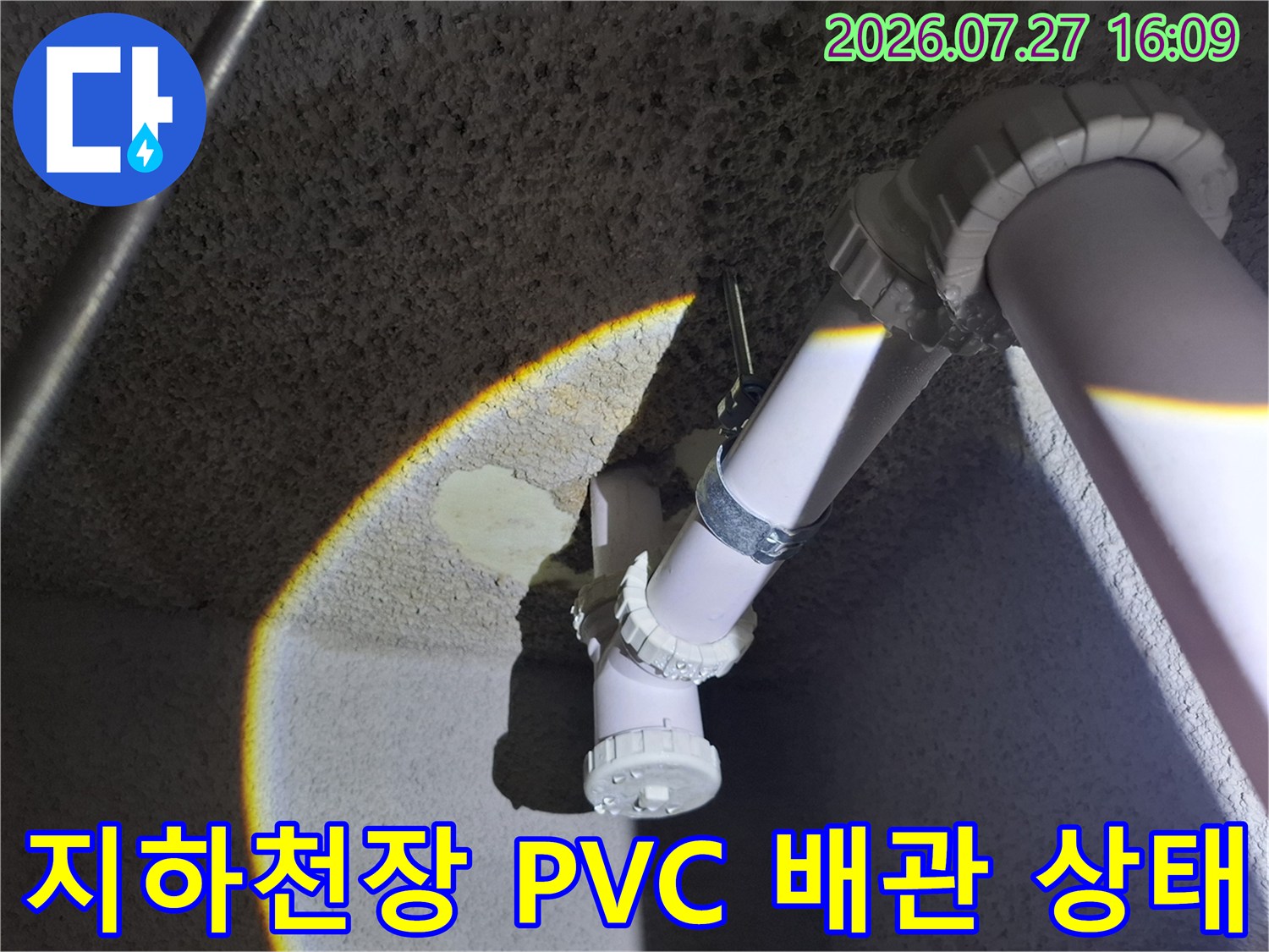 거친 콘크리트 질감의 지하 천장에 설치된 흰색 플라스틱 하수 배관-연결 부위 사진