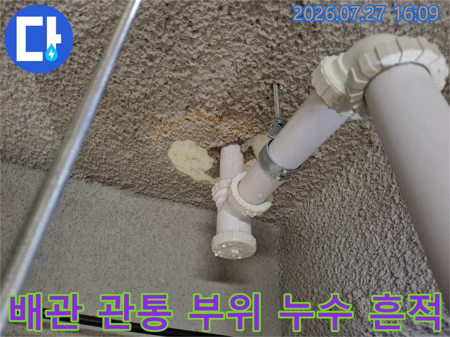 거친 콘크리트 천장에 설치된 흰색 배관과 연결부-주변 습기 흔적