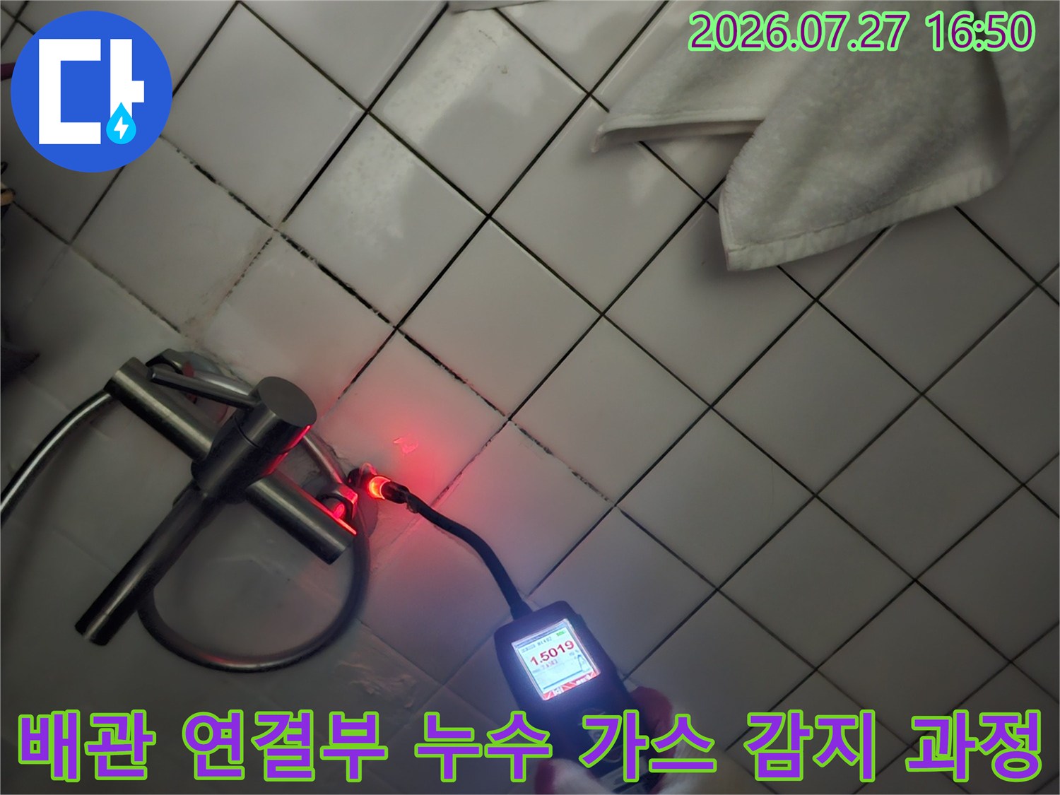 작업자가 장갑을 착용하고 천장 배관에 탐지기를 대어 수치를 읽고 있는 모습