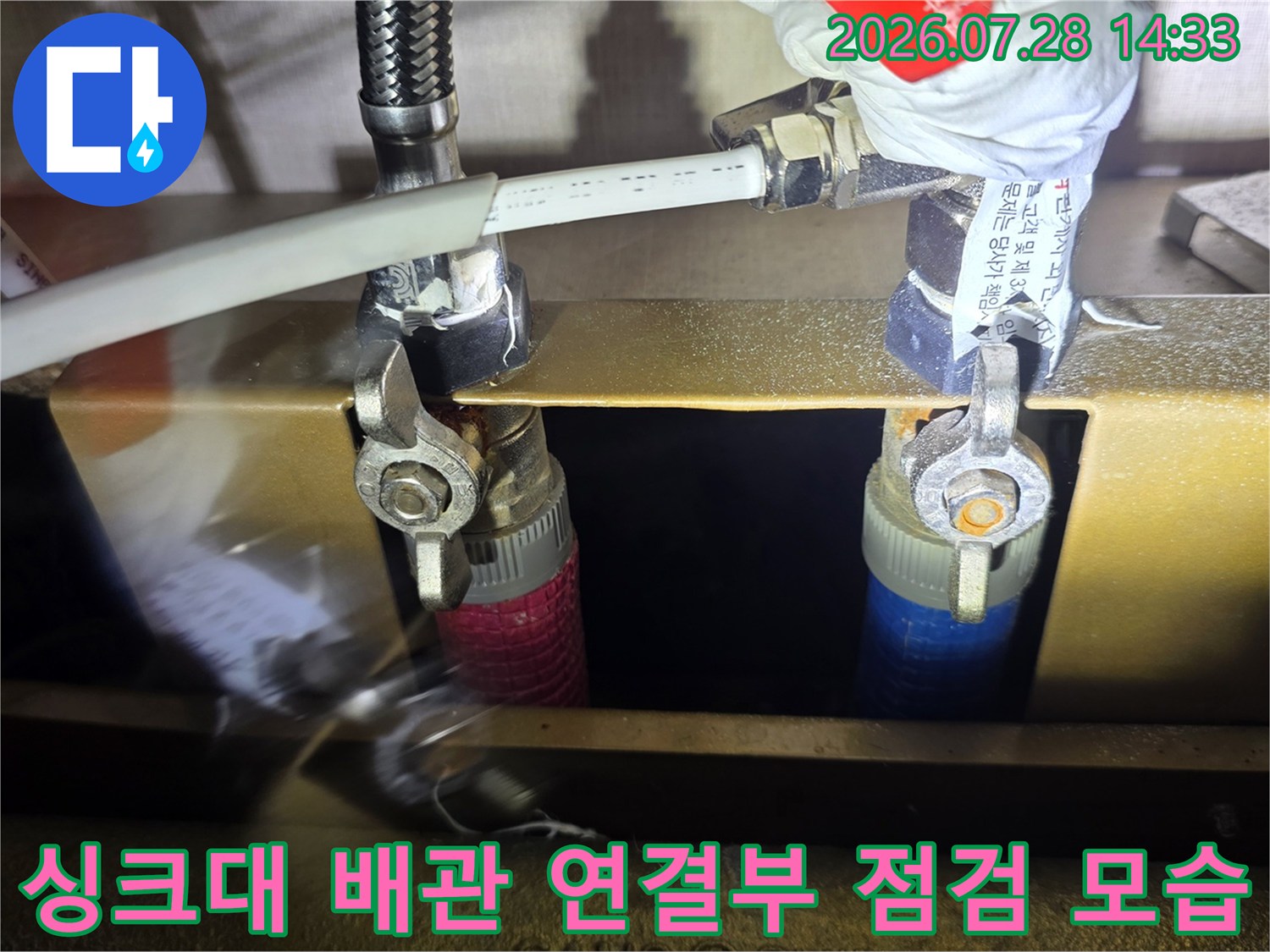 싱크대 하부의 스테인리스 주름관과 분배기 연결 부위를 몽키스패너로 확인하고 있는 모습