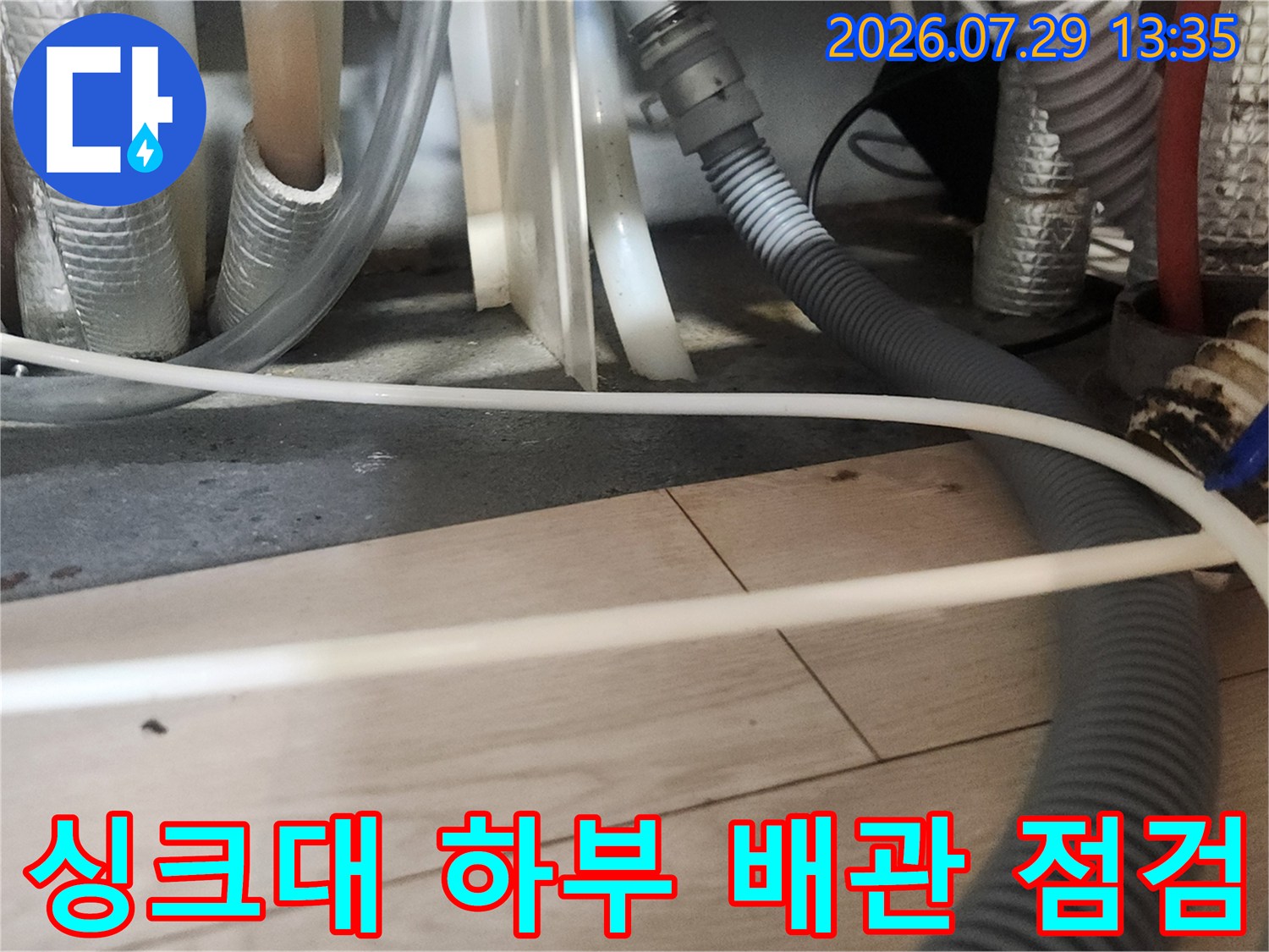 내시경 장비를 활용하여 싱크대 밑에 노출된 여러 개의 배수 호스를 정밀하게 살피는 장면입니다.