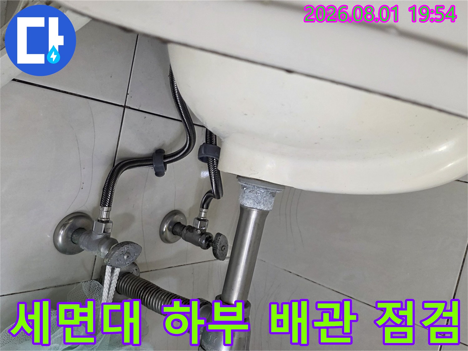 세면대 아래쪽의 노출된 금속제 배관과 연결 부위를 점검하는 모습