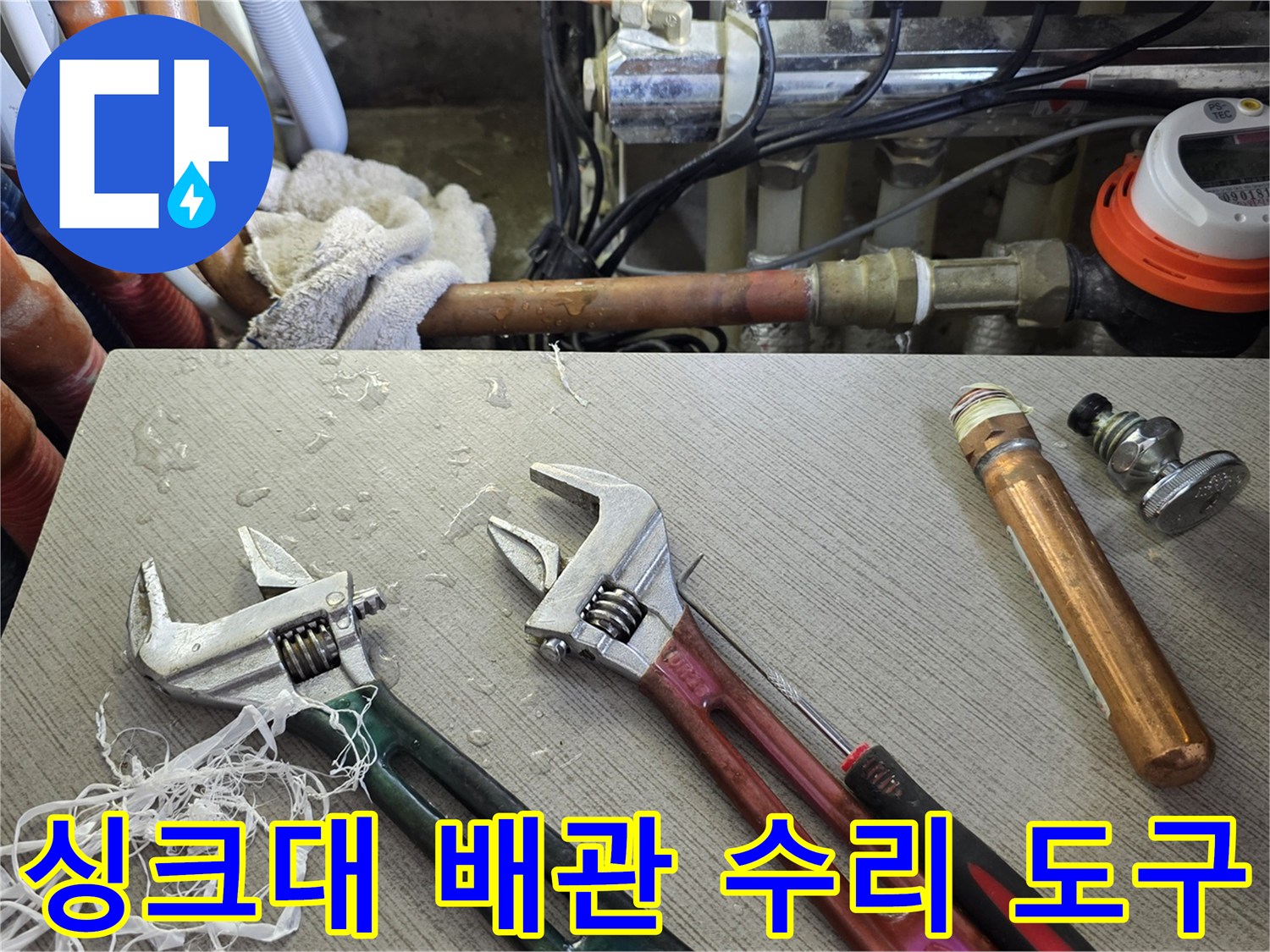 몽키스패너와 배관 부속품이 놓여 있는 작업 현장 사진입니다.
