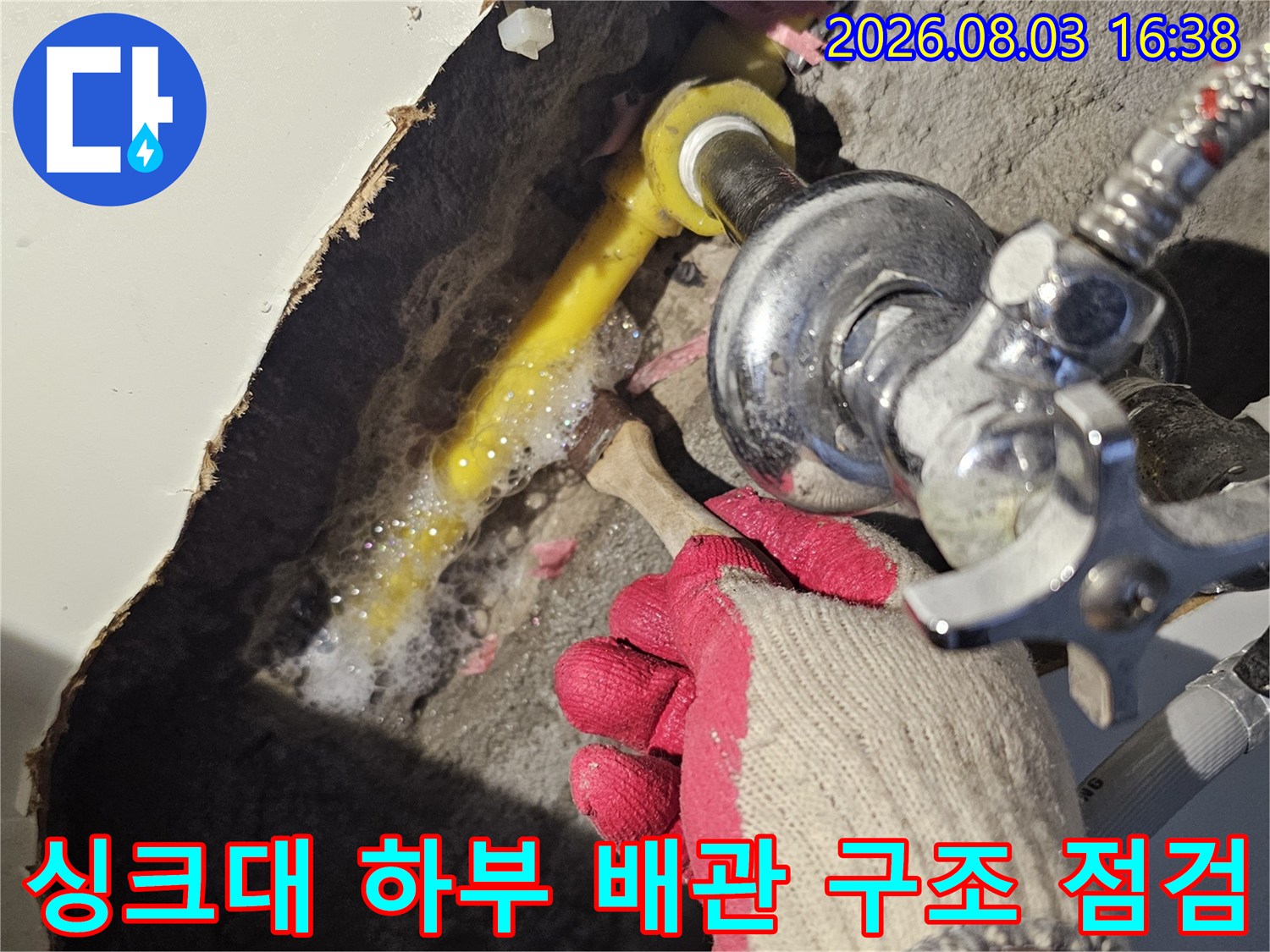 작업자가 장갑을 끼고 싱크대 아래 파헤친 바닥 속 배관 연결부를 상세히 살피는 모습