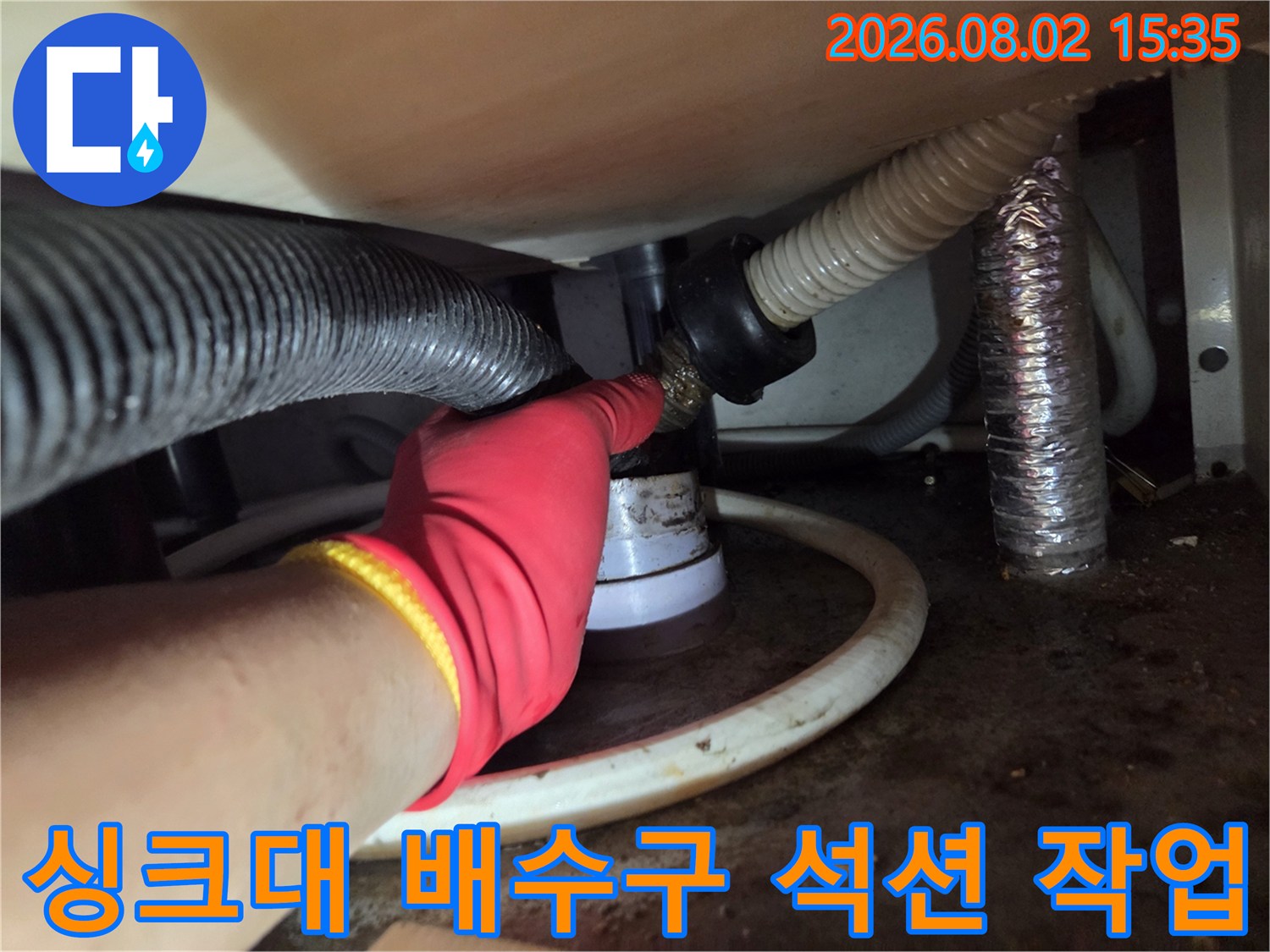 장갑을 착용한 작업자가 싱크대 아래 배수관에 석션 장비를 연결하여 이물질을 제거하는 모습