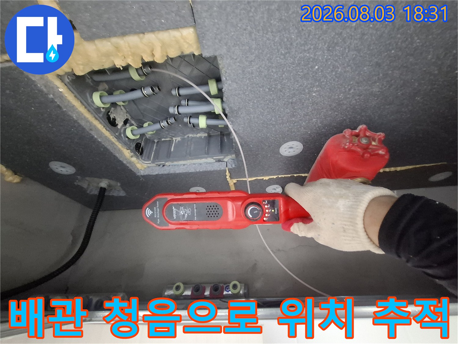 청음 장비와 파색의 장갑을 착용한 전문가가 천장 속 배관을 점검하는 모습