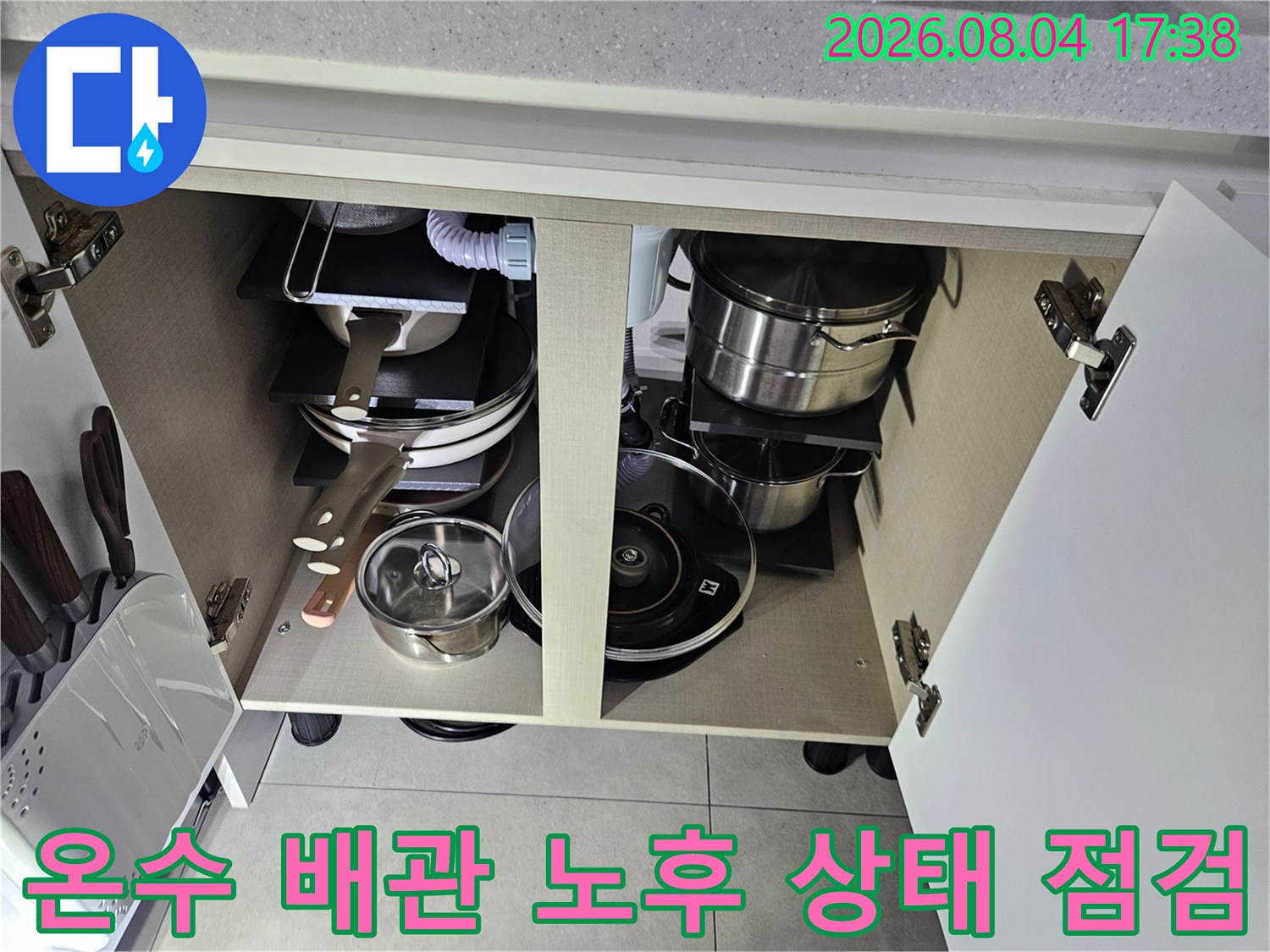 싱크대 아래 공간에 배치된 여러 개의 가전과 얽혀있는 온수 배관을 확인하는 장면