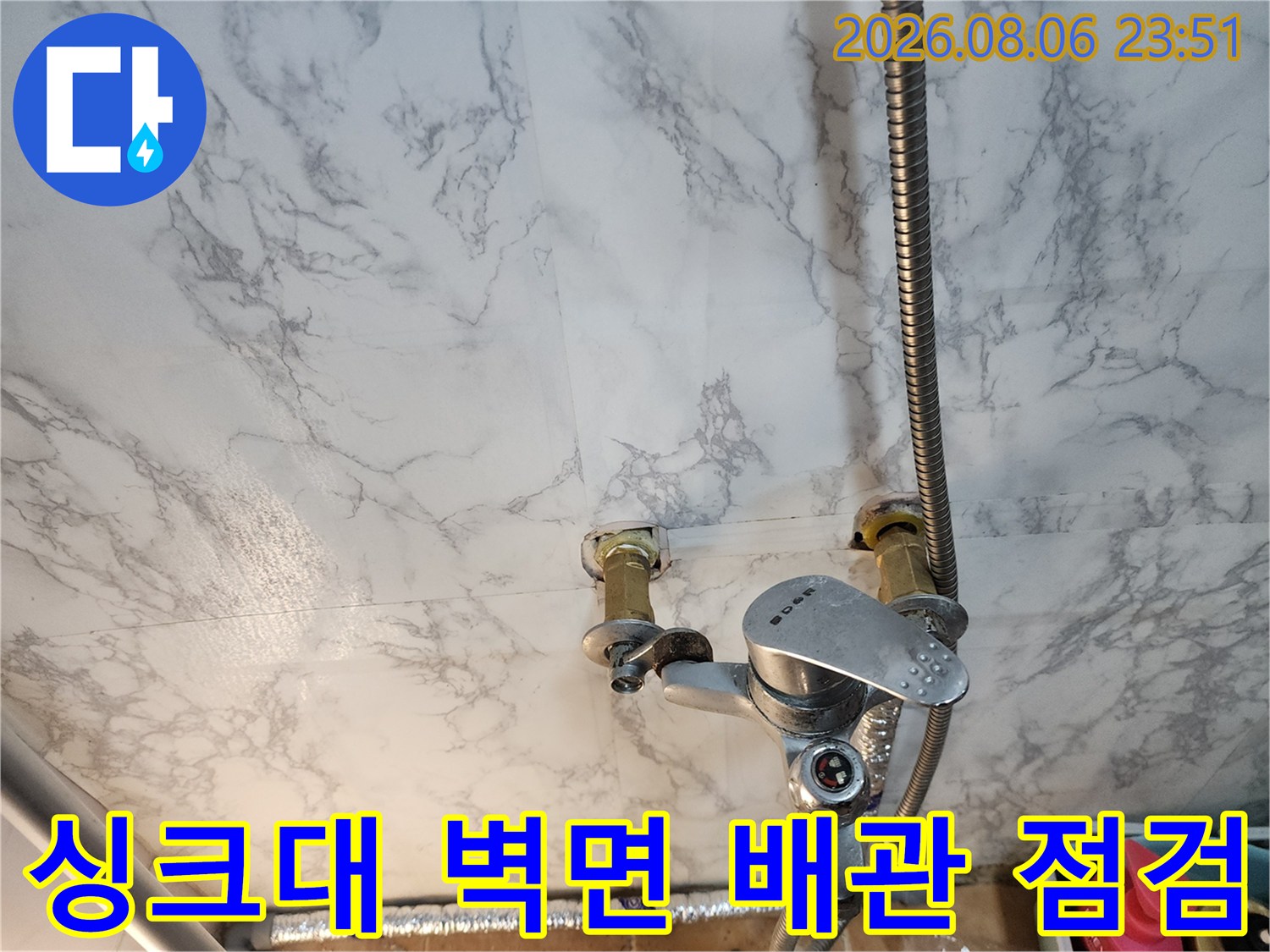대리석 패턴 벽면에 설치된 은색 수전과 연결 배관의 모습입니다.
