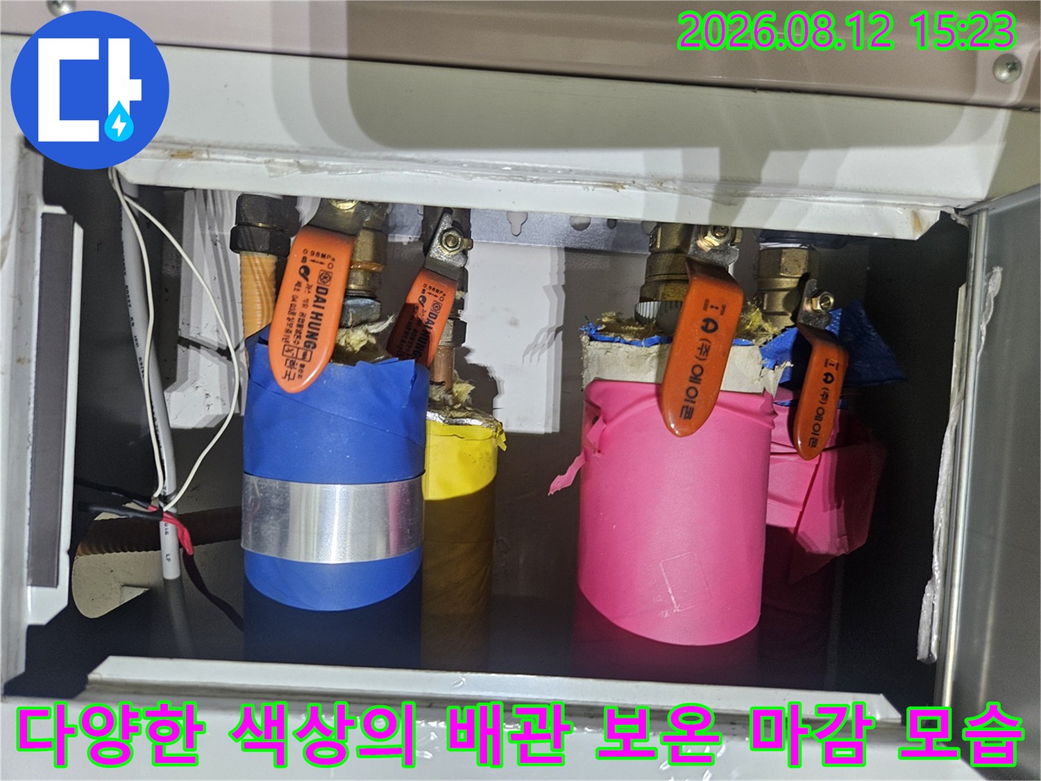 주황색 밸브가 달린 파란색과 분홍색 배관 보온재가 나란히 배치된 설비함 내부