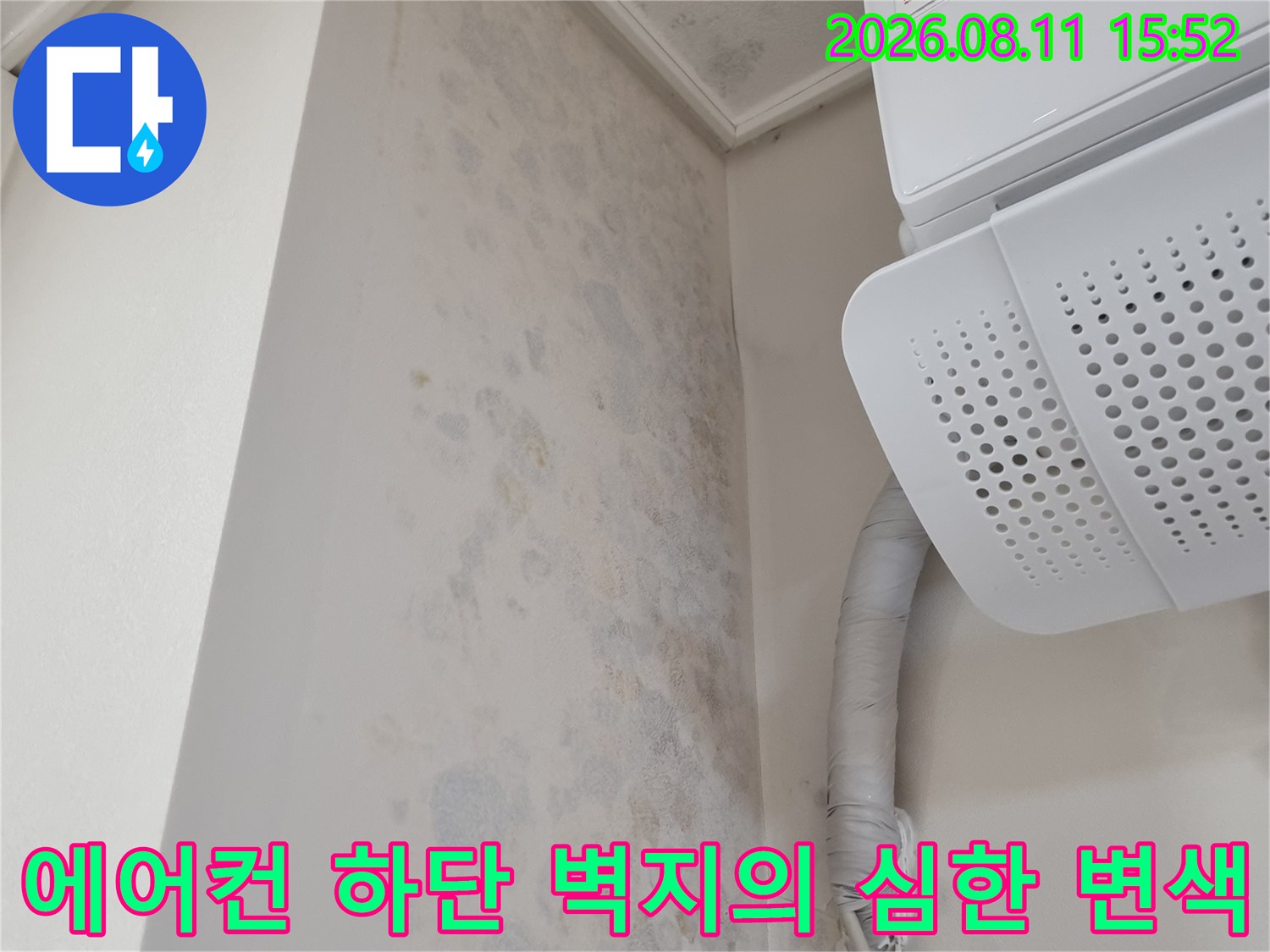 흰색 에어컨 본체와 회색 보온재 배관 아래로 푸른색과 갈색 얼룩이 섞인 벽면 모습