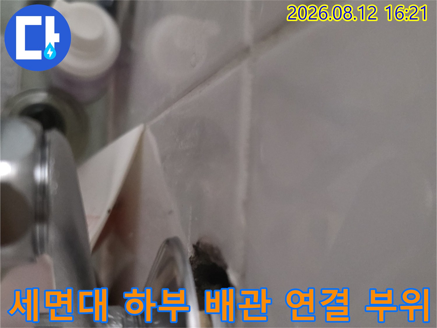욕실 세면대 아래쪽의 금속제 배관 연결 부분과 천장 마감재 사이의 틈새 모습