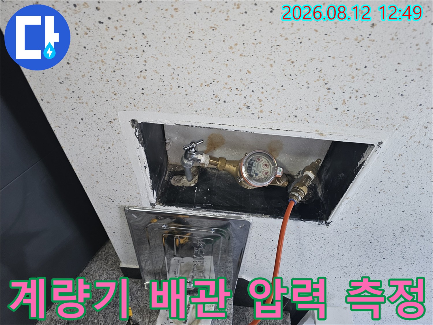 수도 계량기에 연결된 주황색 호스와 배관 부속들의 모습입니다.
