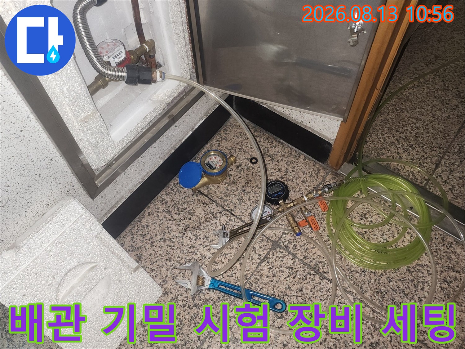 점검구를 통해 드러난 배관에 압력 측정 호스가 연결된 상태-옆에 전등과 렌치가 놓임