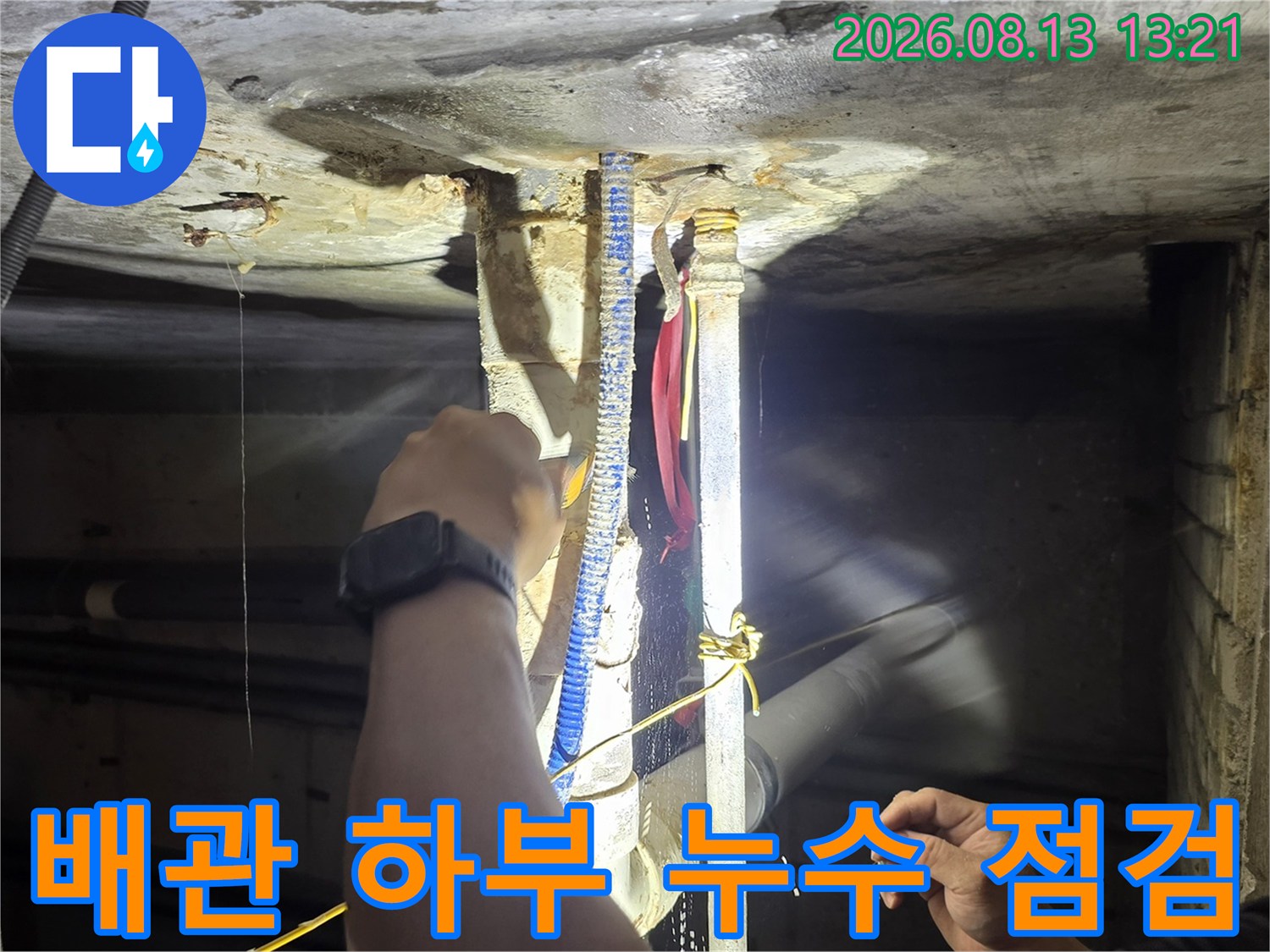 어두운 천장 배관 구조를 손전등으로 비춰 오염 부위를 찾는 모습입니다.
