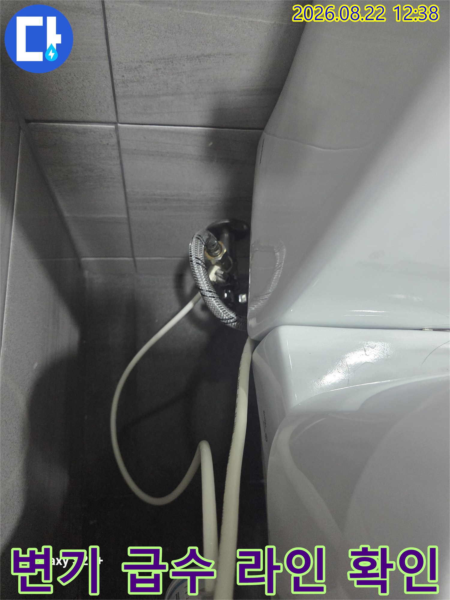 벽면 타일과 연결된 변기용 급수 밸브 및 호스 사진입니다.