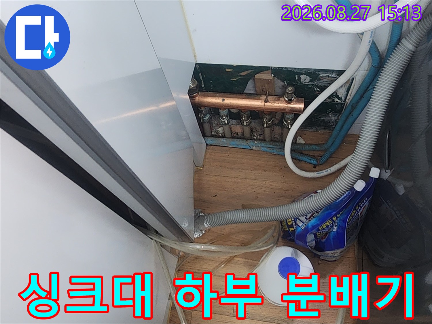 복잡하게 얽힌 보일러 배관과 투명 호스들이 싱크대 아래쪽에 설치되어 있습니다.
