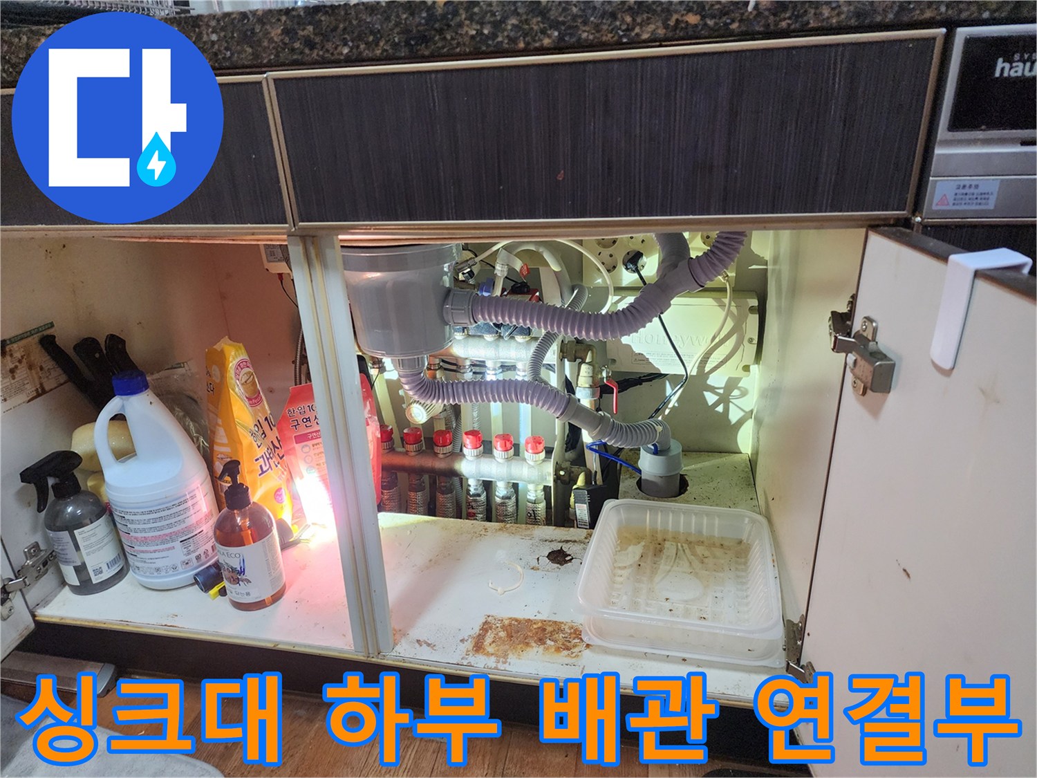 싱크대 밑에 설치된 에어컨 배수 호스와 다양한 배관들
