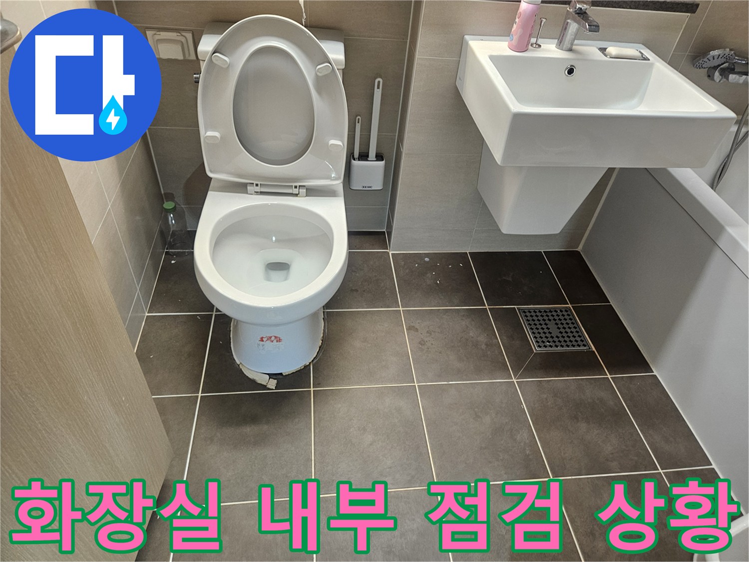 회색 타일 벽면과 흰색 양변기가 설치된 욕실의 전체적인 구도입니다.