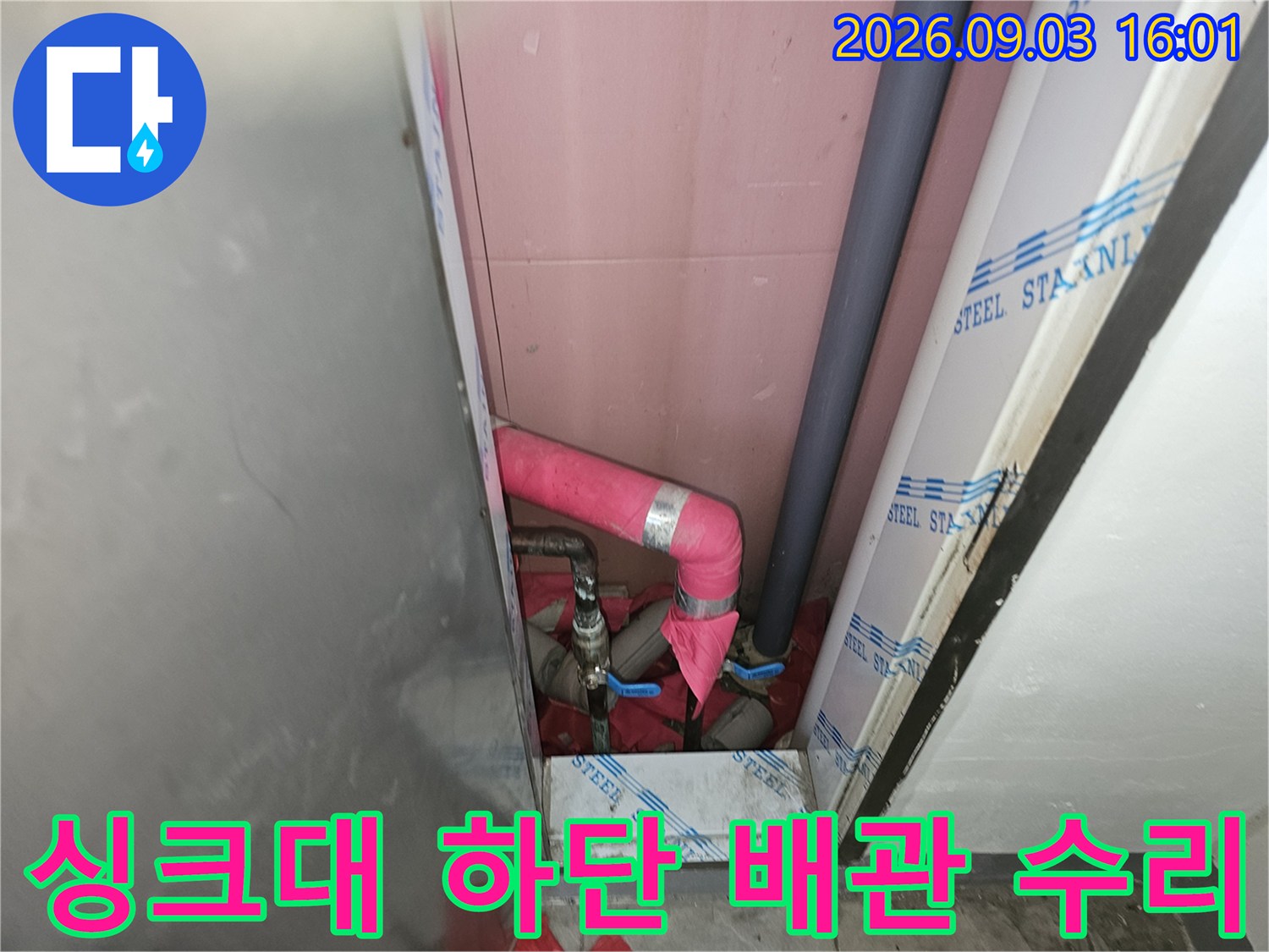 분홍색 단열재가 씌워진 배관이 싱크대 하부 공간에 설치되어 있습니다.