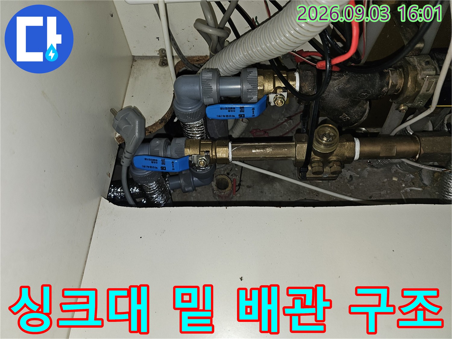 싱크대 하부 공간에 노출된 파란색 밸브와 금속제 배관의 모습입니다.