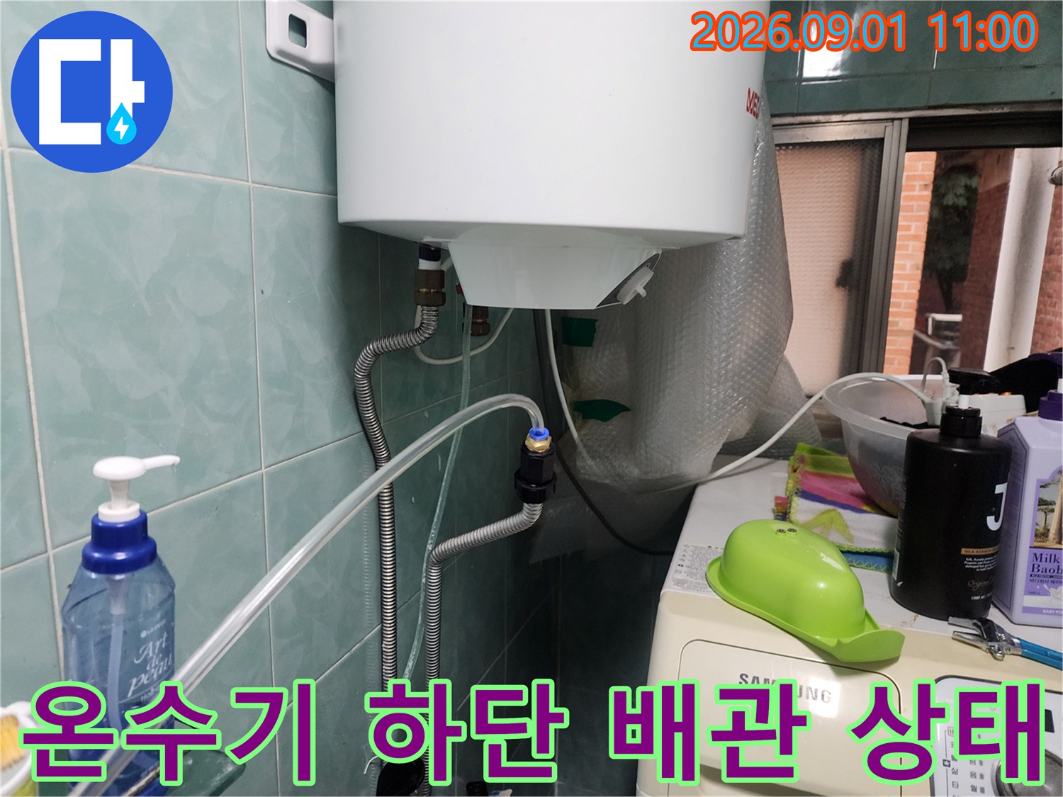 온수기 본체 아래로 연결된 금속 호스와 밸브 부위의 모습입니다