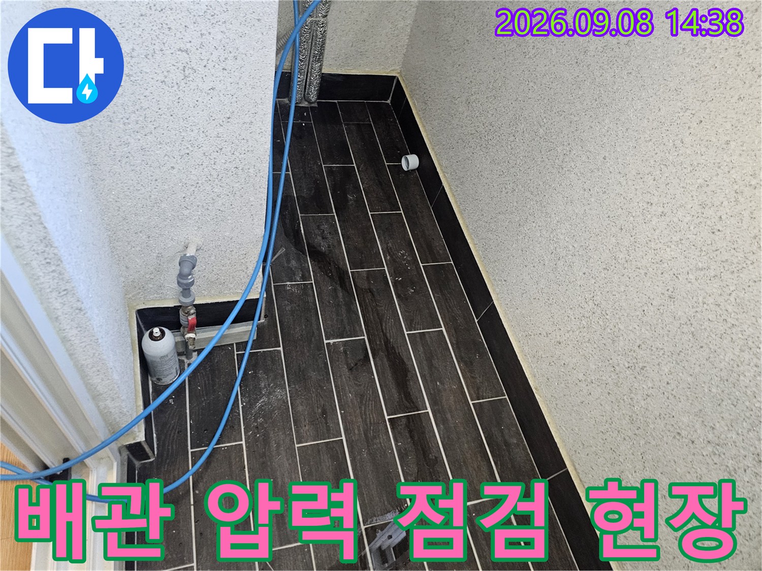 어두운색 타일 벽면에 연결된 파란색 호스와 압력 측정 장비 모습