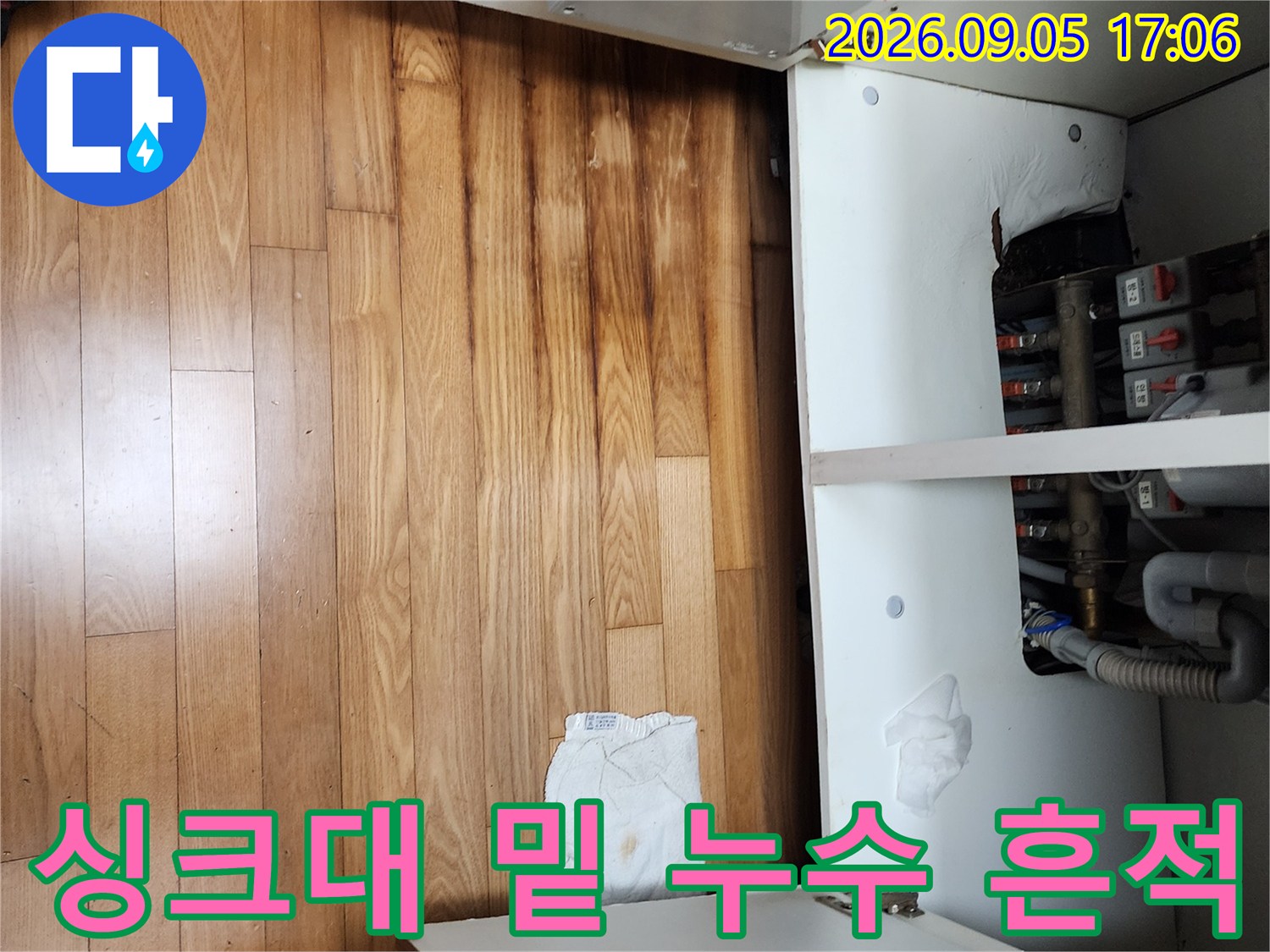 싱크대 하부장 내부 배관 주변의 습기와 마루 변색 상태를 보여줍니다.