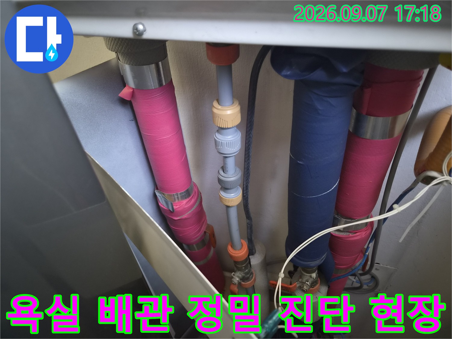 다양한 색상의 배관과 밸브가 설치된 공간의 누수 여부를 점검하는 장면입니다.