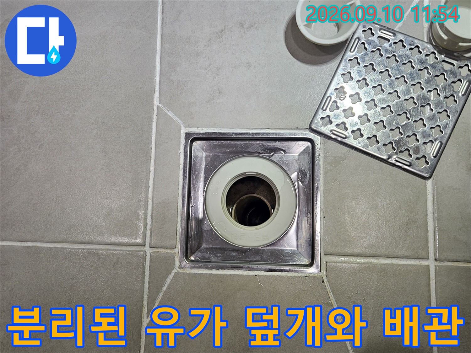 타일 바닥에 놓인 유가 덮개와 노출된 배수구 배관의 근접 촬영