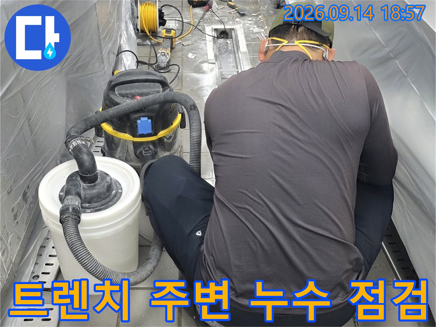 바닥 배수 트렌치 인근의 누수 지점을 확인하기 위해 청소 장비와 보양재를 갖추고 작업 중인 현장입니다.