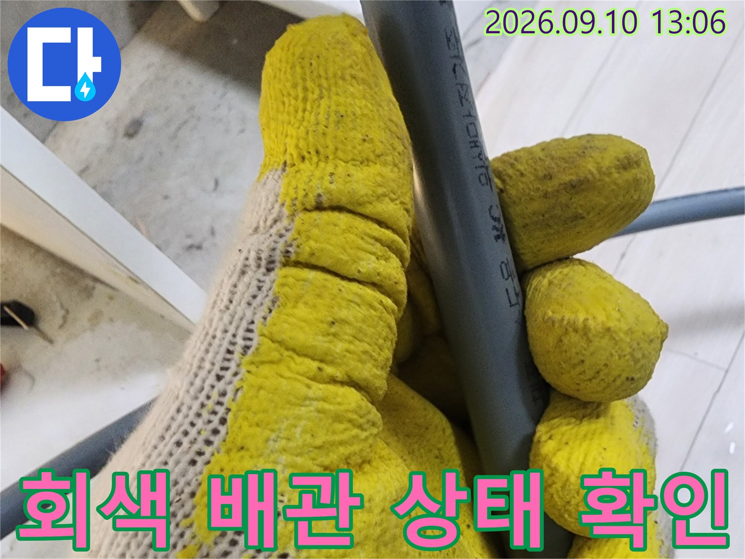 작업자가 회색 수도 배관을 손으로 잡고 점검하는 장면