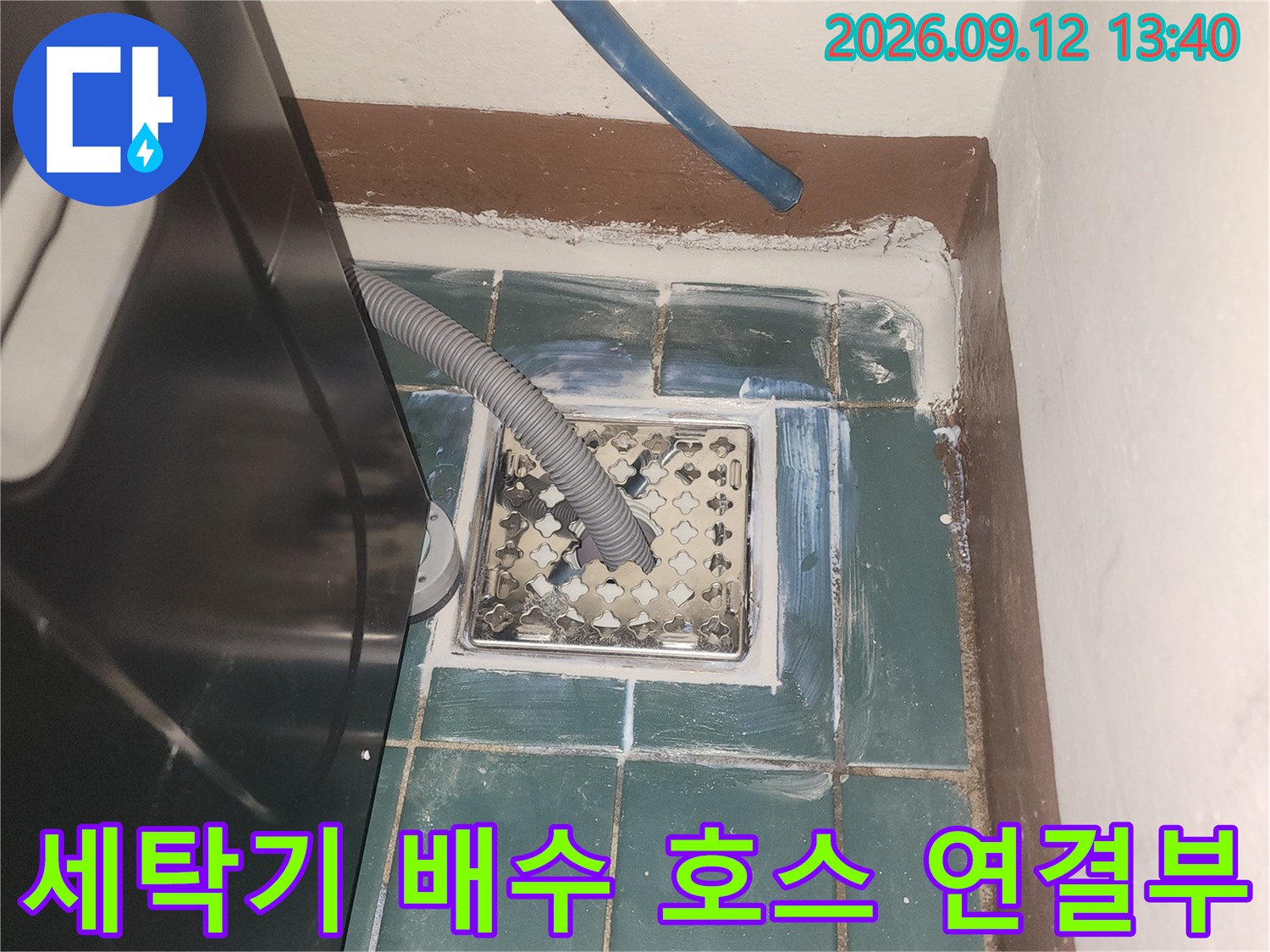 세탁실 배수구에 연결된 회색 배수 호스와 주변 타일입니다.