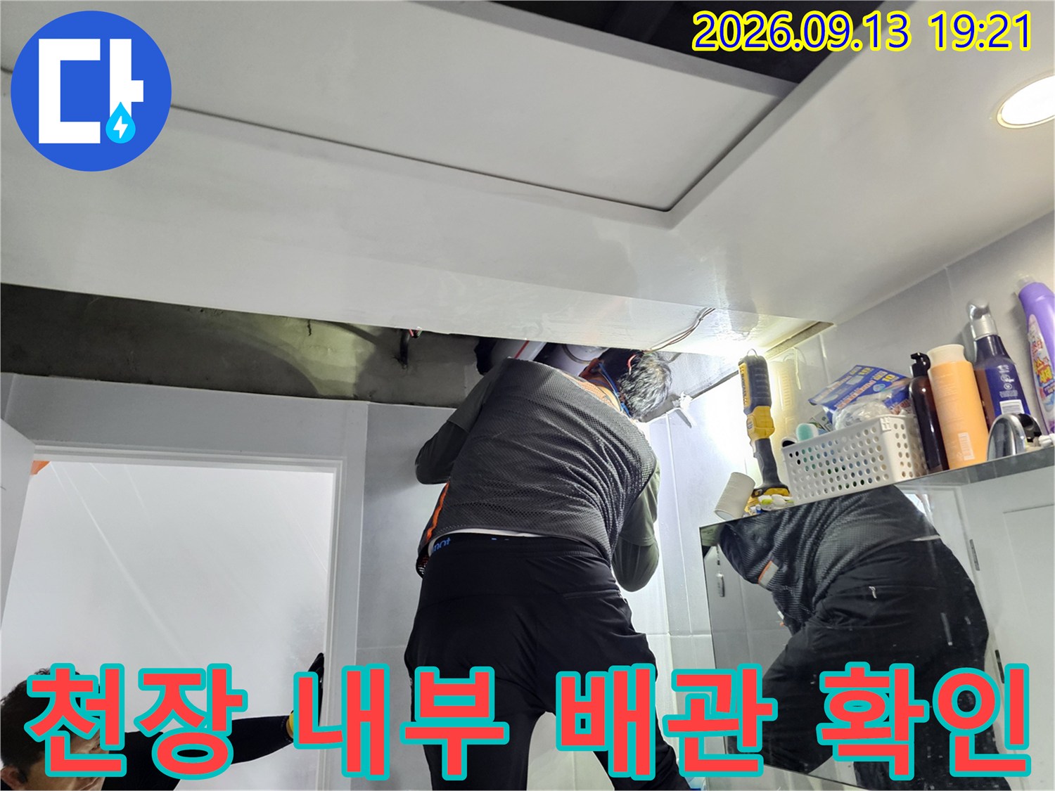 손전등을 사용하여 천장 점검구 내부의 배관 연결 상태를 면밀히 조사하고 있습니다.