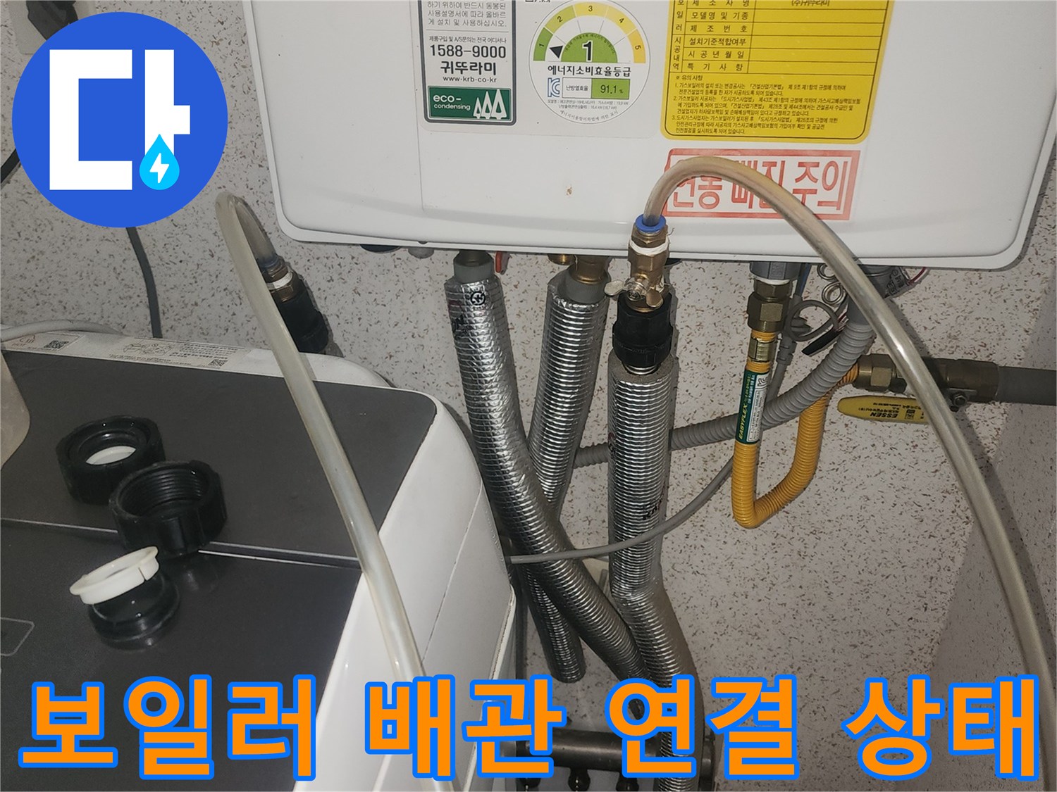 보일러 하단에 연결된 은색 주름관과 노란색 가스관의 모습입니다.