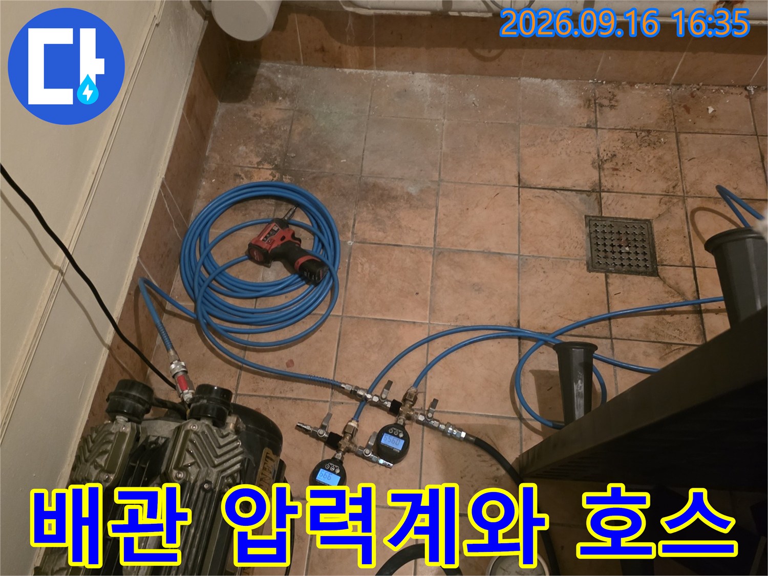 타일 바닥에 배치된 디지털 게이지와 연결된 파란색 공압 호스입니다.