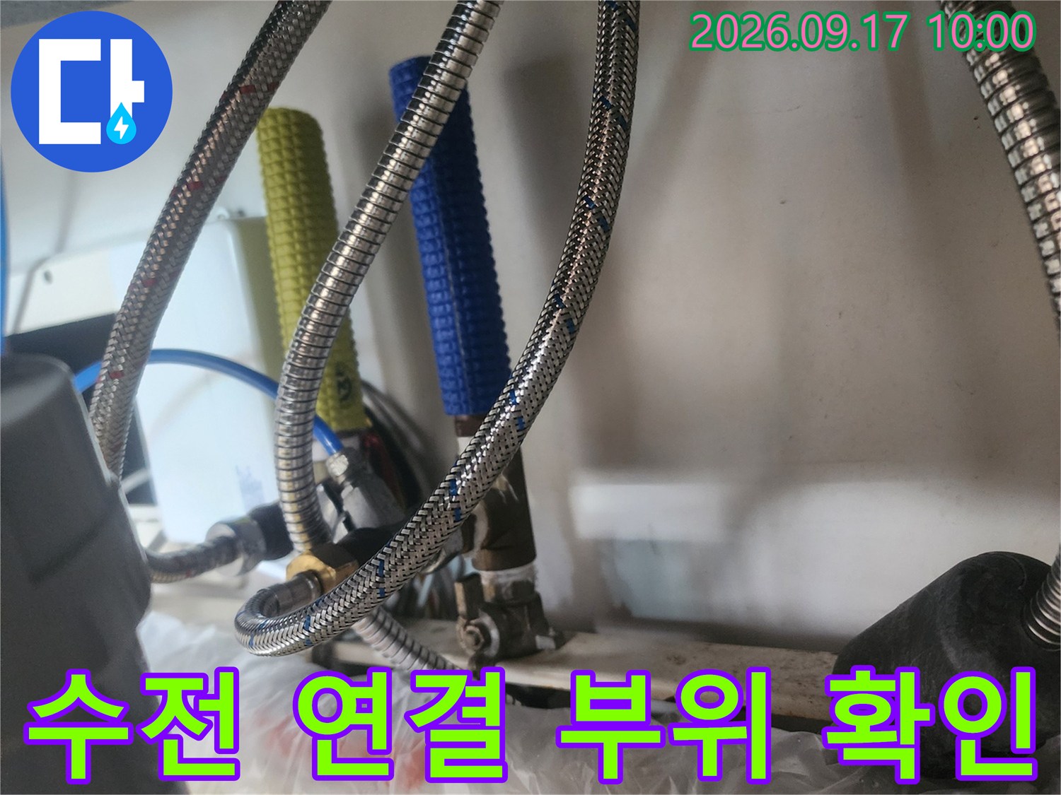 금속 호스와 보온 배관이 복잡하게 얽혀 있는 싱크대 하부 점검 모습입니다.